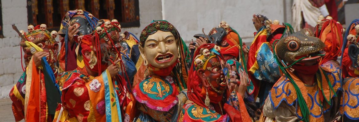 Maskentänzer mit traditionellen Gewändern und Masken bei der Darstellung eines spirituellen buthanesischen Tanzes.