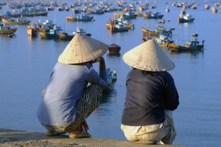 Zwei Einheimische beobachten den lebhaften Bootsverkehr an der Küste von Vietnam.