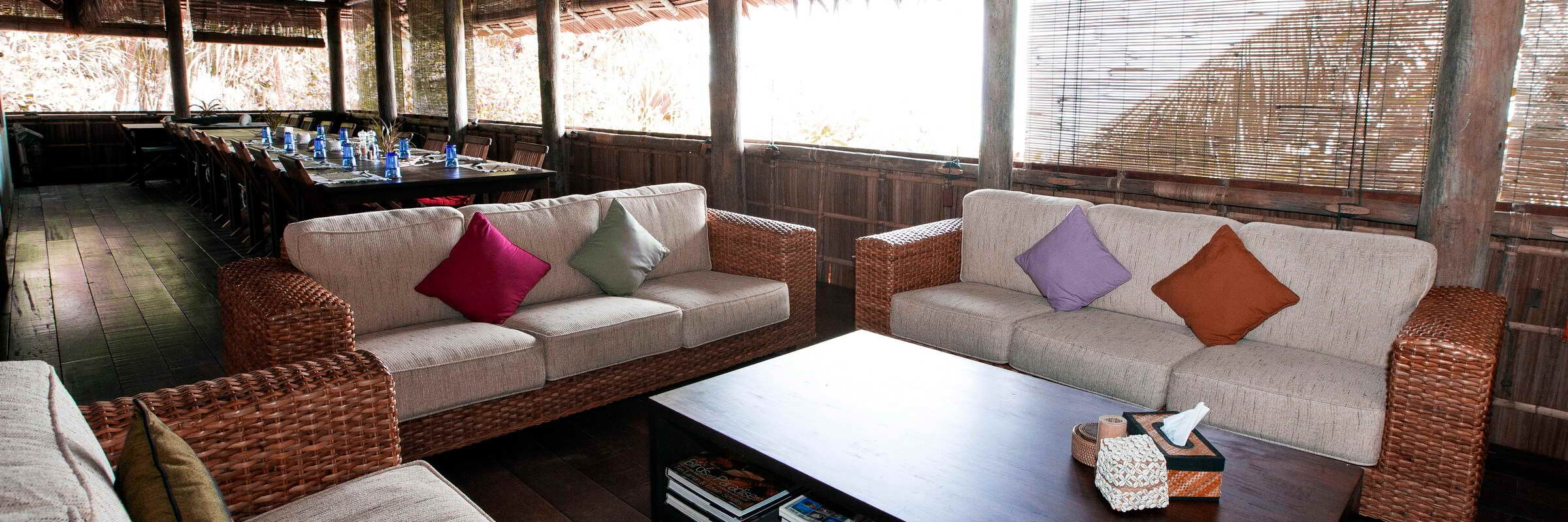 Der offene Lounge- und Restaurantbereich im Sorido Bay Resort mit hohen Holzdecken, bequemen Holzsitzgruppen und Blick auf das türkisfarbene Wasser der Lagune und die üppige Dschungellandschaft im Hintergrund.
