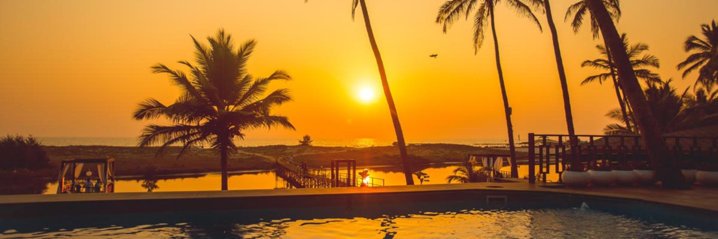 Der im Garten gelegene Außenpool des Riva Beach Resort mit Liegestühlen bietet einen hervorragenden Blick auf den abendlichen Sonnenuntergang.