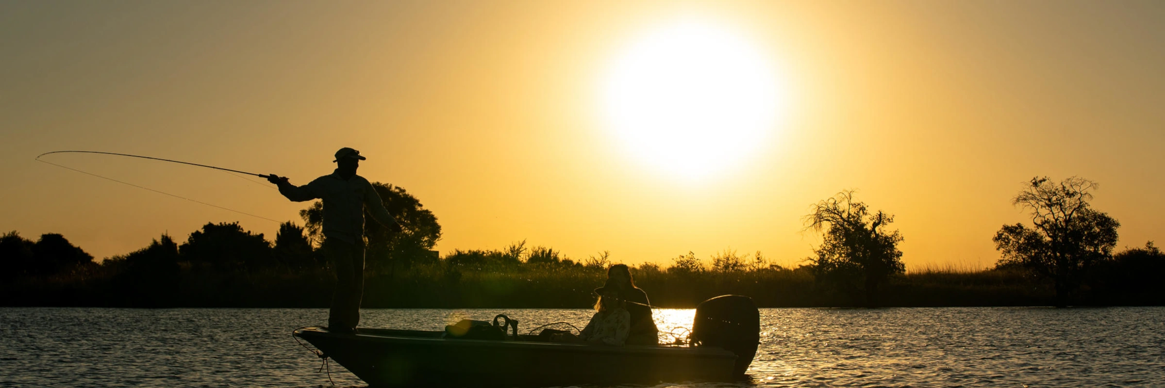 Silhouette eines Anglers auf einem Boot beim Fischen vor einem intensiv goldenen Sonnenuntergang in Afrika.