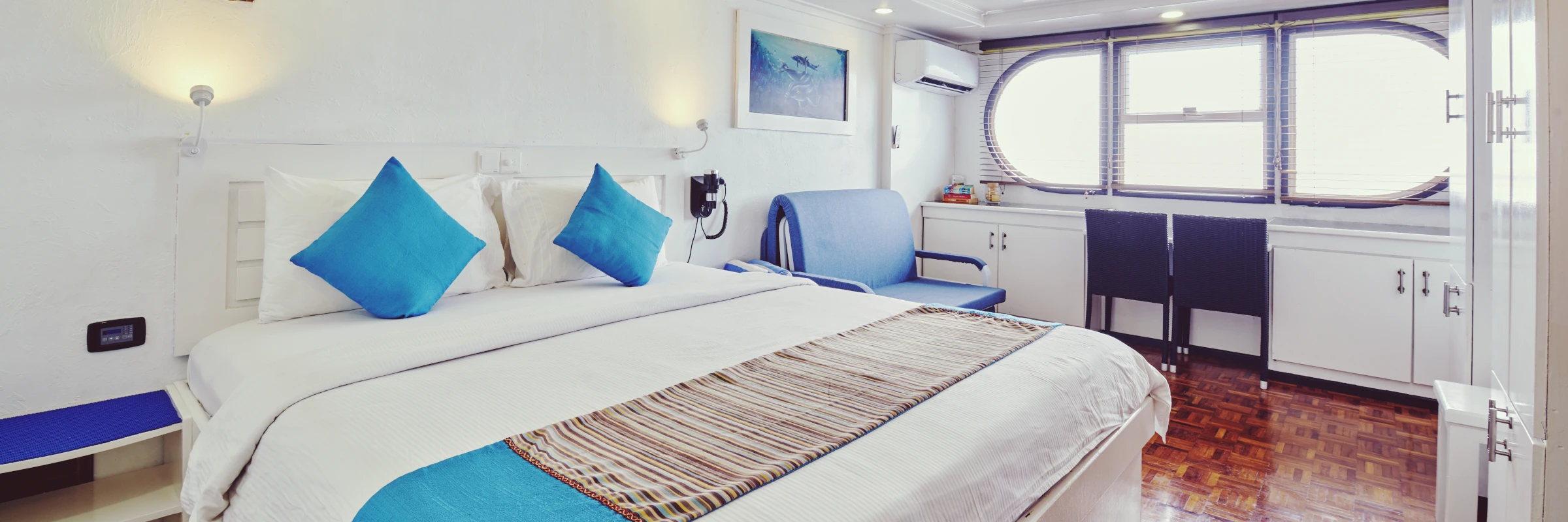 Helle und geräumige Luxuskabine an Bord des Tauchschiffs Horizon&nbsp;III mit einem großen Doppelbett, blauen Kissen, gemütlicher Sitzecke und Fenstern.