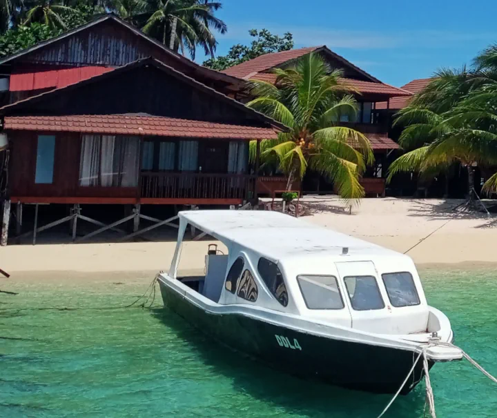 Tauchboote der Derawan Dive Lodge am weißen Sandstrand von Pulau Derawan in Ost-Kalimantan, Indonesien, vor türkisfarbenem Meer.