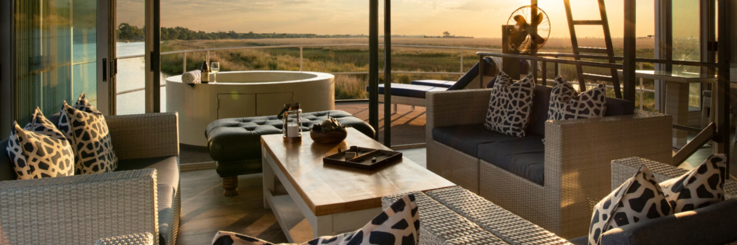 Die edle Außenlounge auf dem Deck eines Luxus-Hausboots mit gemütlichen Sofas und einem Whirlpool im warmen Licht des Sonnenuntergangs.