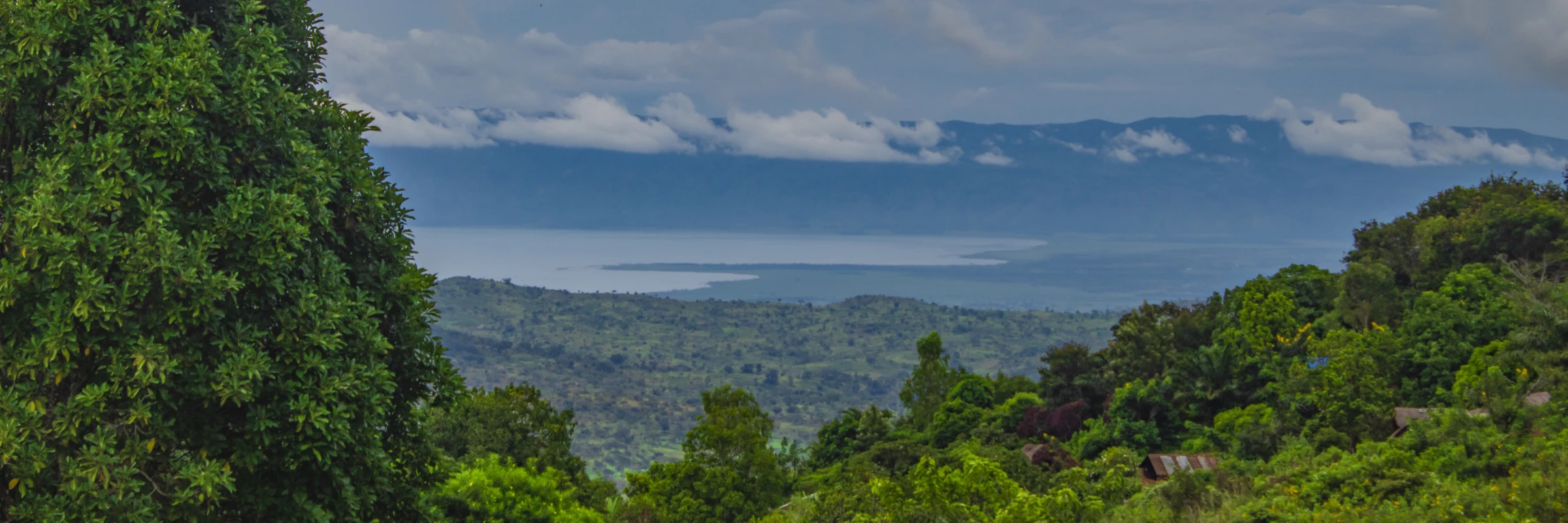 Panoramablick auf den Lake Kivu in Ruanda umgeben von grünen Bergen und Hügeln unter Wolken