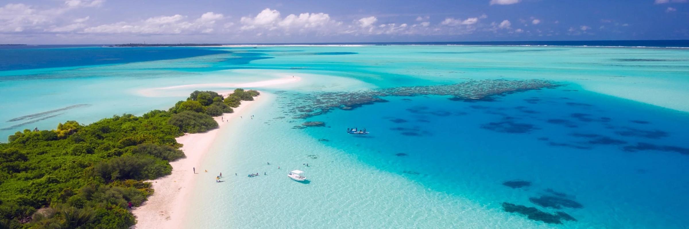 Luftaufnahme einer maledivischen Sandbank mit tropischer Vegetation, umgeben von türkisblauem Wasser und einem großen Korallenriff.