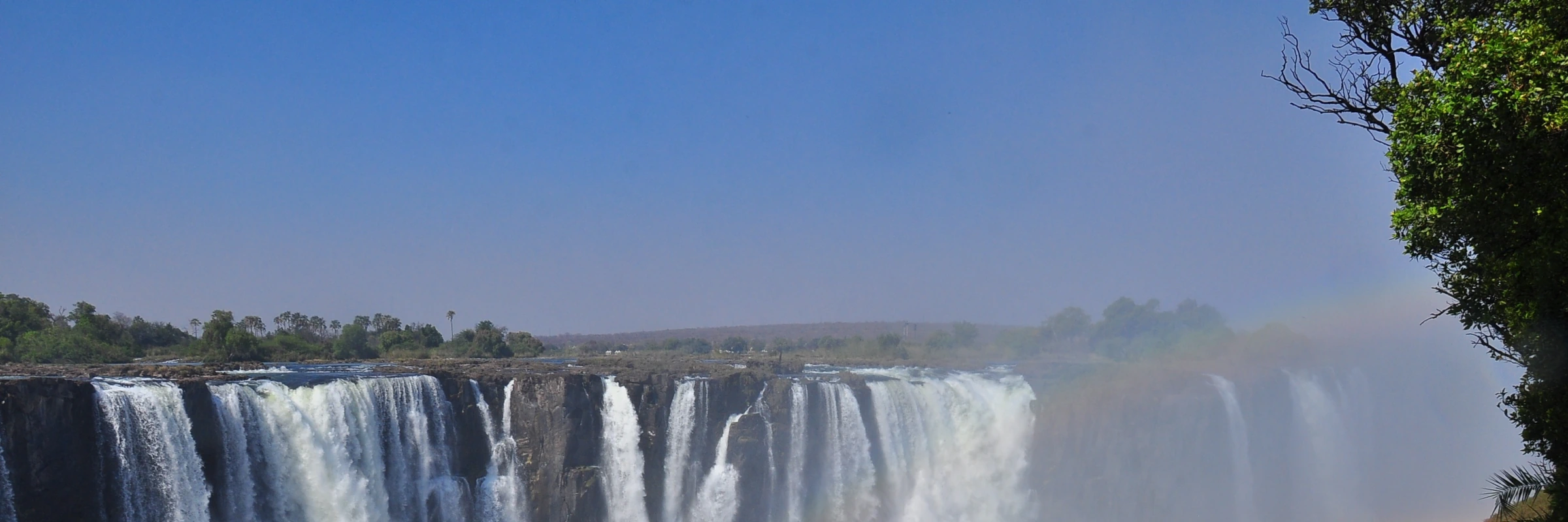 Spektakuläre Panoramaaufnahme der Victoriafälle mit Gischt und Regenbogen in Afrika