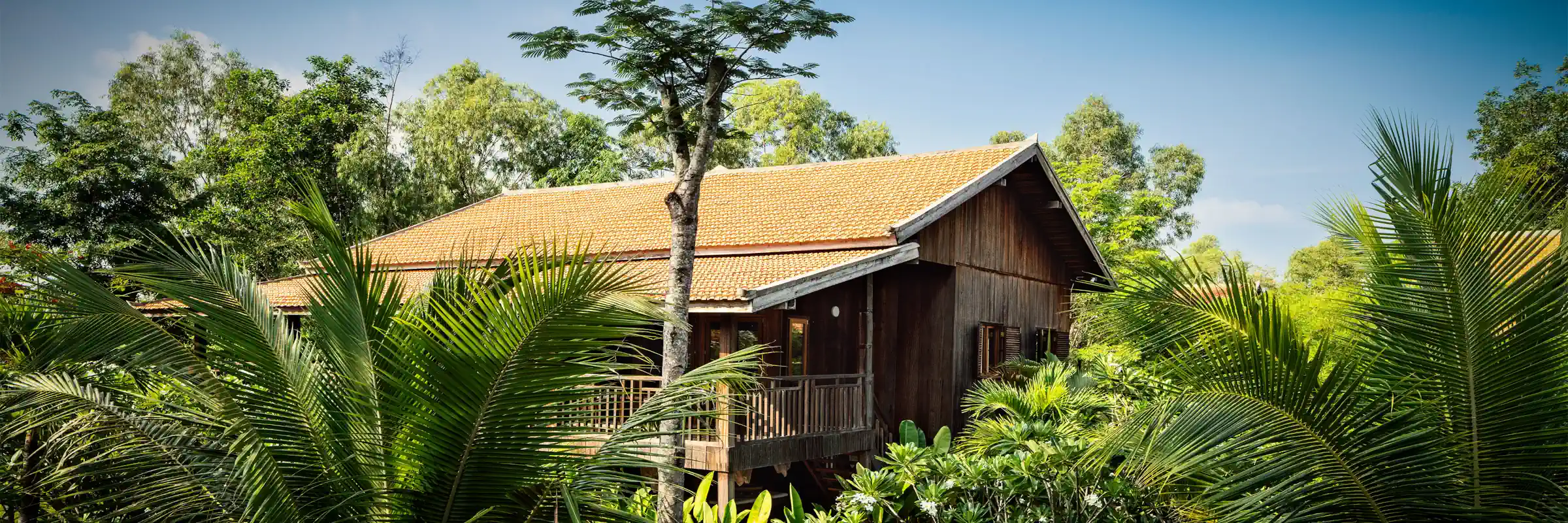 Traditioneller Khmer-Holzbungalow umgeben von tropischen Palmen im Farmhouse Resort & Spa.