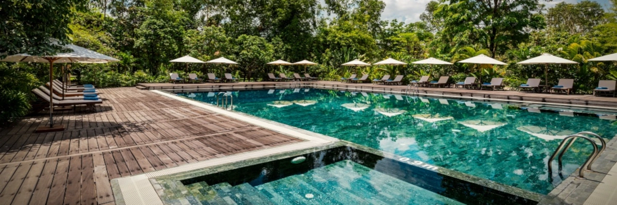 Salzwasserpool mit großzügigem Holzdeck, Liegestühlen und Sonnenschirmen im Farmhouse Resort & Spa in Kambodscha.