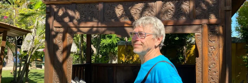 Wolfgang Mühlbauer, Reiseexperte von Reisefieber, vor einem traditionell geschnitzten Holzpavillon auf Bali.
