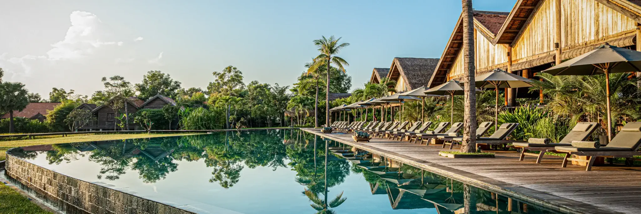 Der 50 Meter lange Infinity-Pool des Luxusresorts Zannier Phum Baitang mit Holzliegen und Palmen in Siem Reap.