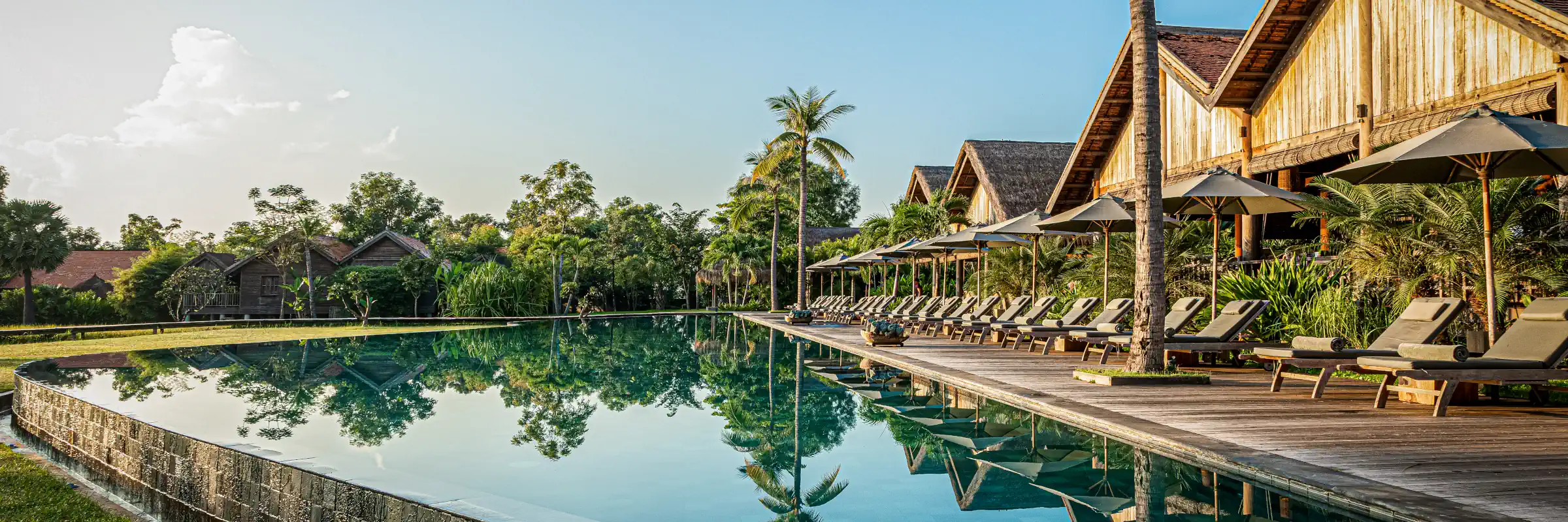 Der 50 Meter lange Infinity-Pool des Luxusresorts Zannier Phum Baitang mit Holzliegen und Palmen in Siem Reap.