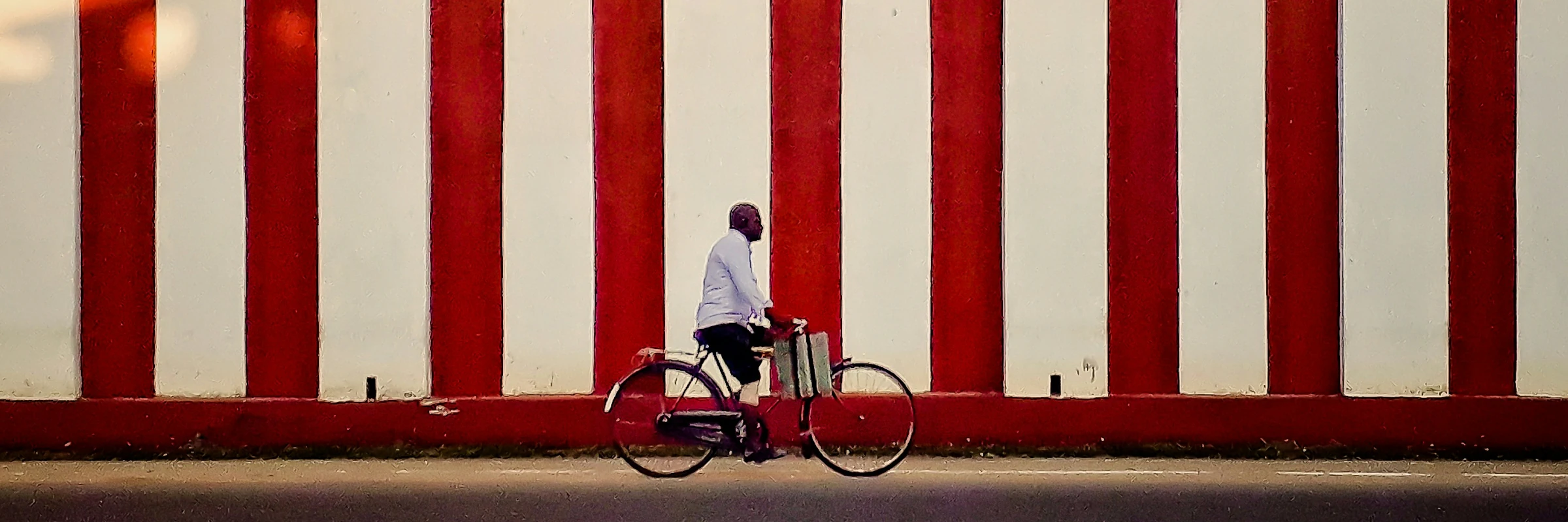 Ein Mann fährt auf einem Fahrrad im Profil an einer auffälligen, vertikal rot-weiß gestreiften Außenwand eines hinduistischen Tempels vorbei.